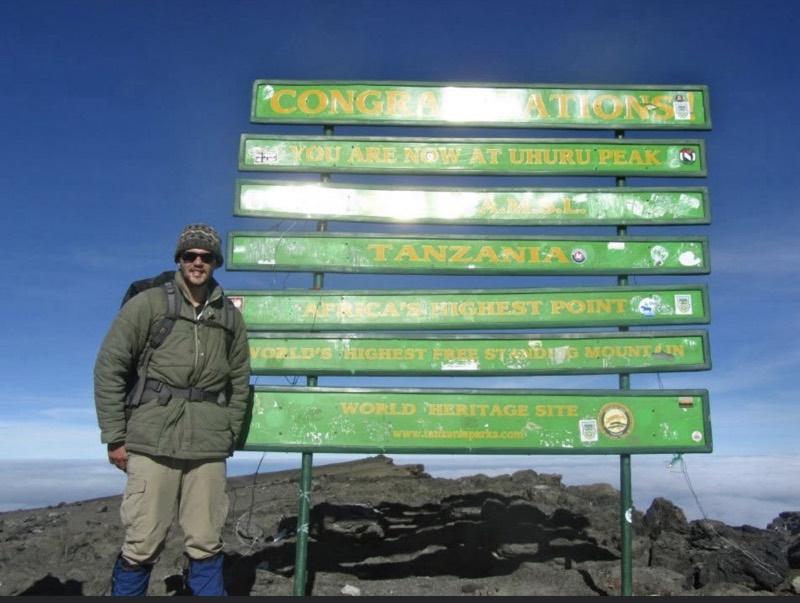 Codie at the Uhuru Peak summit sign on Kilimanjaro, above the cloud line
